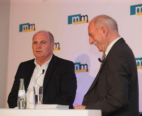 Uli Hoeneß, langjähriger Vorstand und Präsident des FC Bayern und Sportreporter Werner Hansch in einem Podiumsgespräch vor einer m+m Logowand.